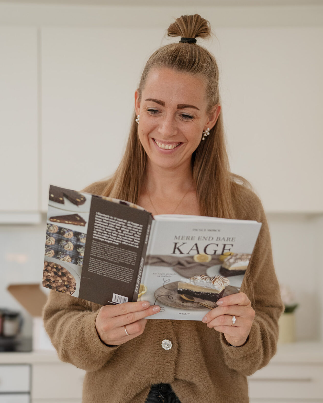 Nicole smiler og holder sin åbne bog Mere end bare kage op foran sig