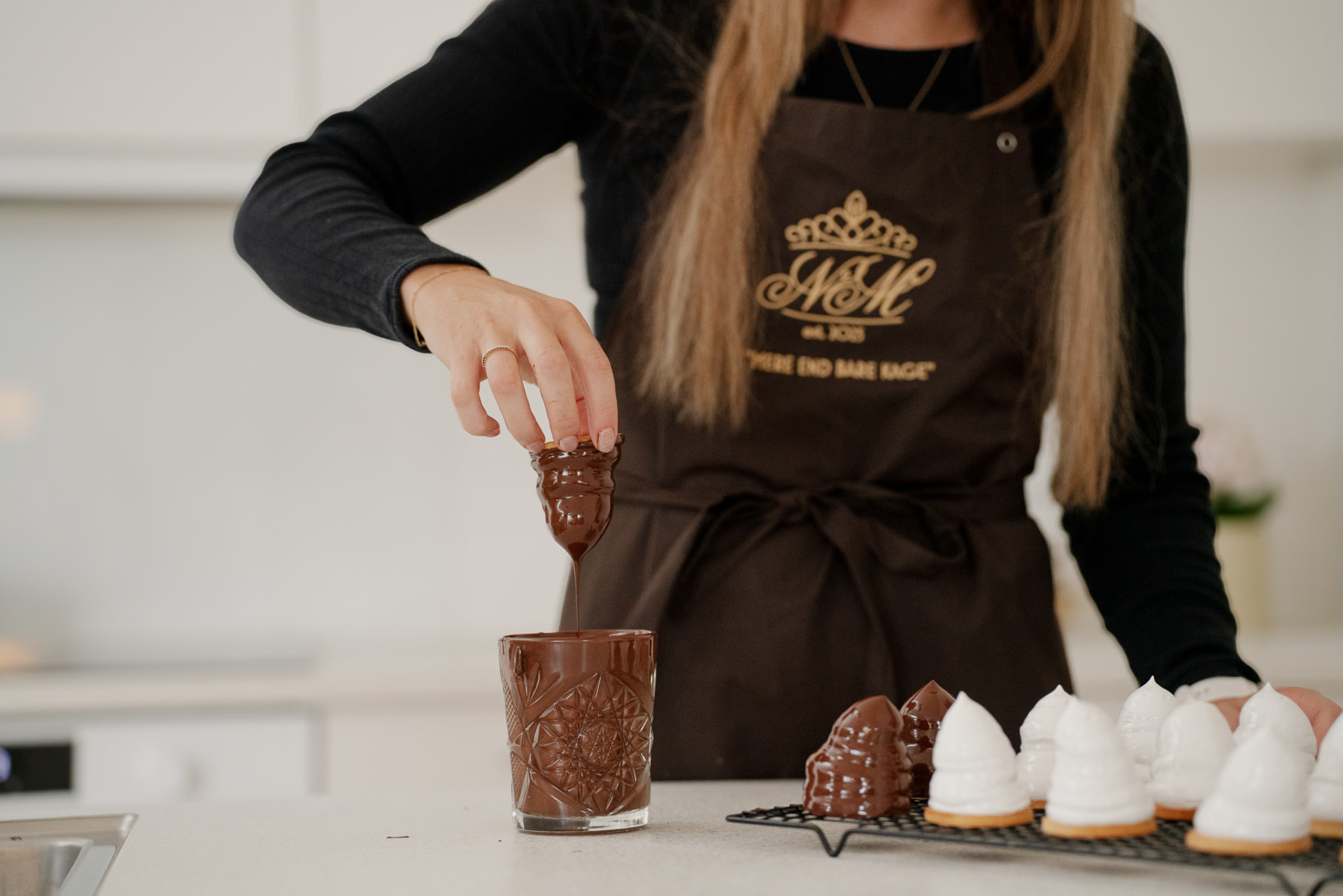 Nicole dypper en flødebolle i smeltet chokolade ved køkkenbordet