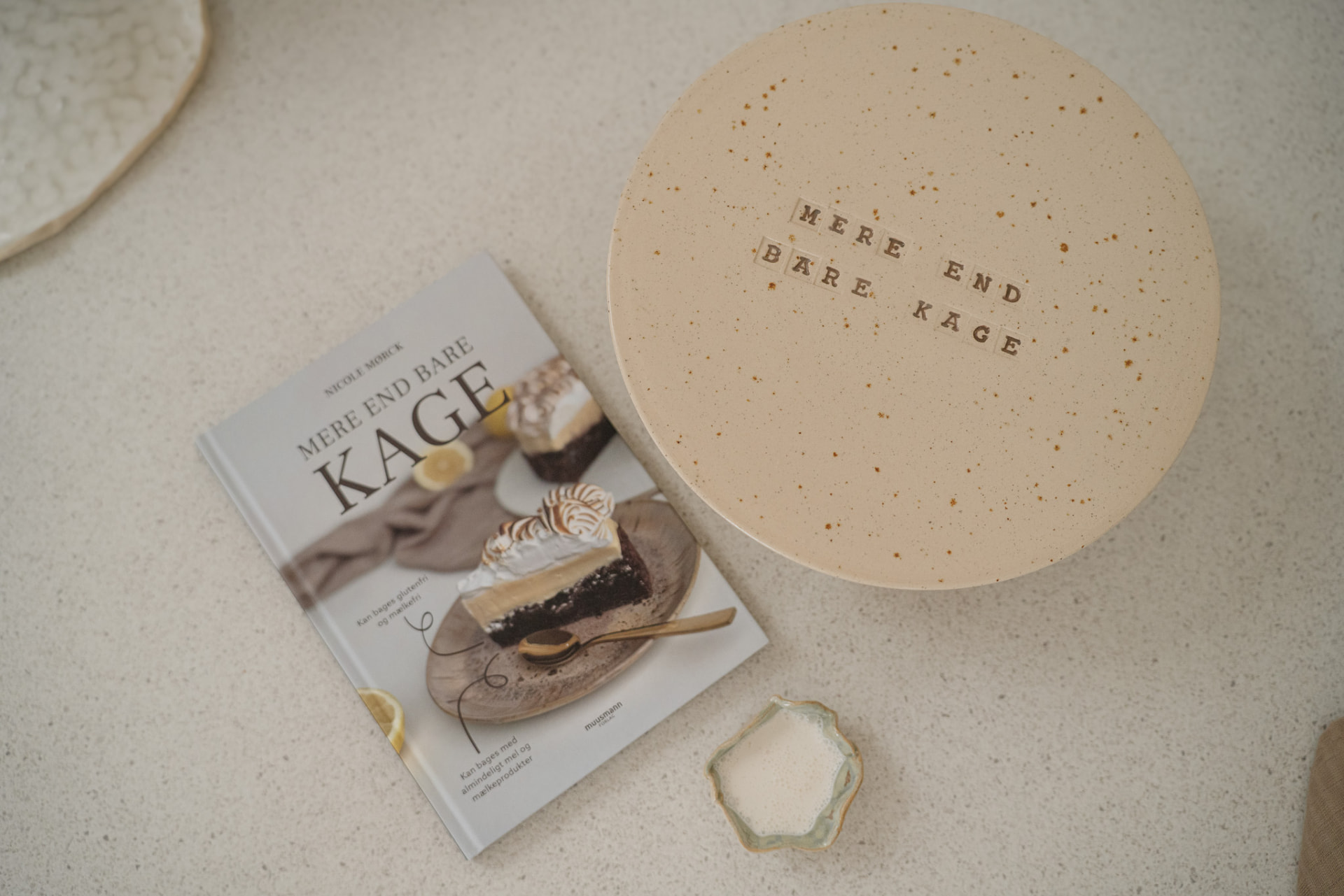 En rund kage med teksten Mere end bare kage skrevet i chokoladebogstaver ved siden af bogen